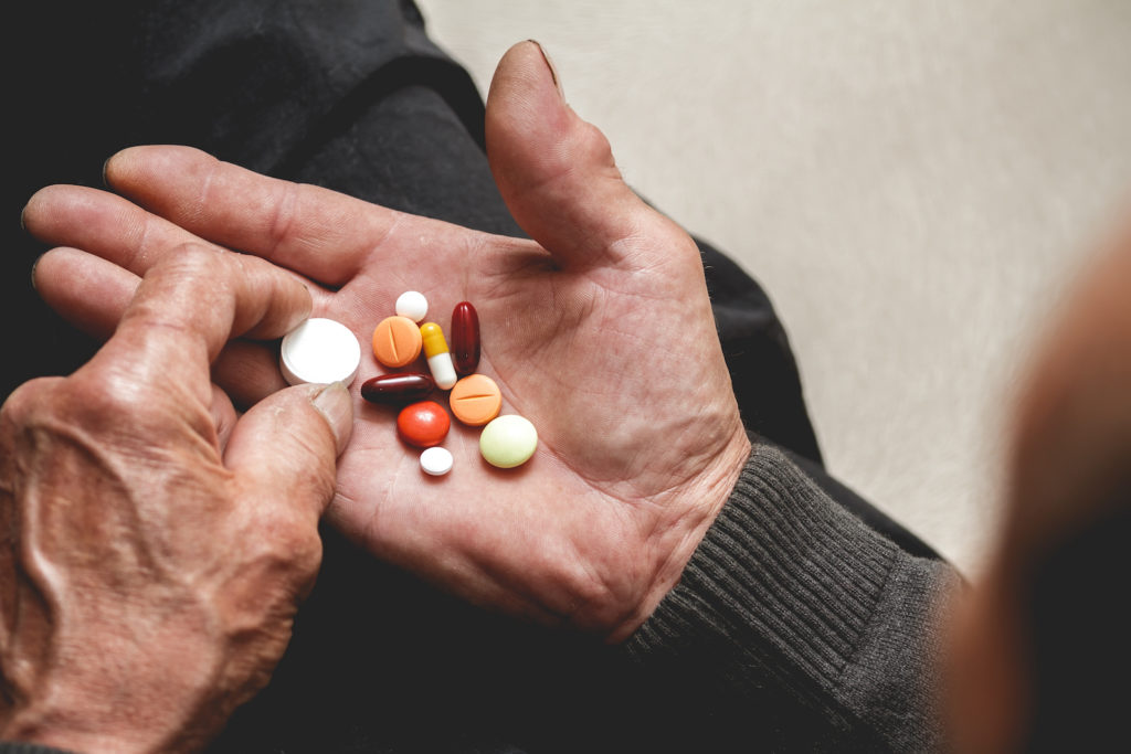 Many multi-colored pills in a Senior's hands; remember to take your meds